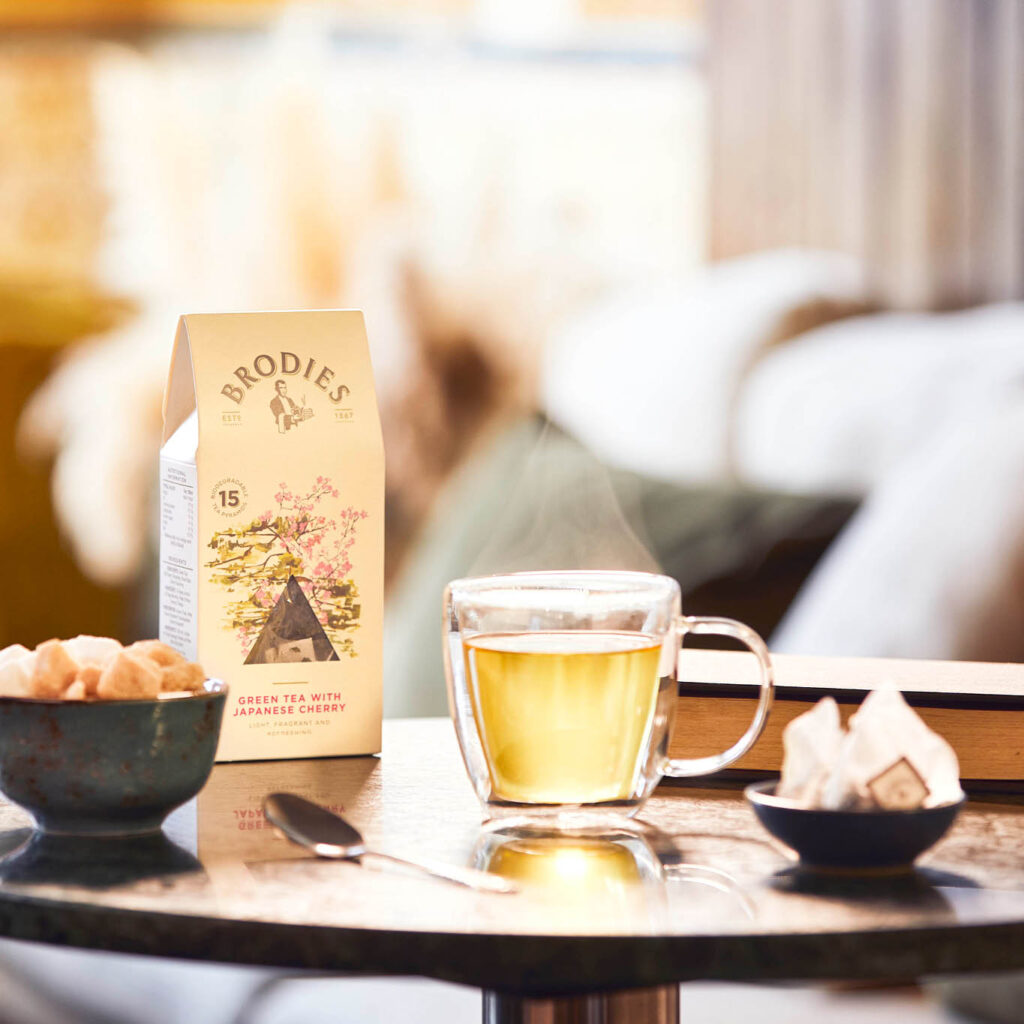 Imagebild Brodies Tee mit Teeglas mit hellem Tee und einer Verpackung mit Teepyramiden