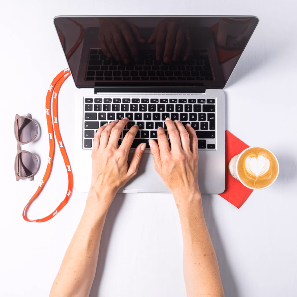 Moodbild von oben mit Händen auf einer Laptop-Tastatur, Sonnenbrille und Kaffee
