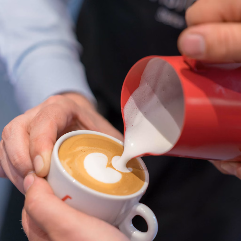 Close-Up-Moodbild Latte Art aus einer roten Milchkanne in einer Tasse